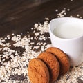 Oatmeal cookies on a background of oats, next to a glass of milk, on vintage board