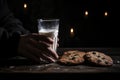 Oatmeal cookies with pieces of chocolate, arranged in a stack, a child& x27;s hand holding a glass of milk on a dark