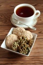 Almond cookies and sugar-coated pumpkin seeds cookies in a square bowl and a cup of black tea on a wooden table. Royalty Free Stock Photo