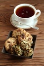 Oatmeal cookies with walnuts and raisins, sugar-coated pumpkin seed cookies in a square bowl and a cup of black tea on a table Royalty Free Stock Photo