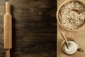 Oatmeal flakes in a wooden bowl with a spoon, ears of wheat, pot of flour, kitchen utensils on the table.