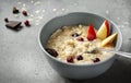 Oatmeal porridge with pieces of fruit, pear, berries, orange, on a gray