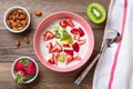 Oatmeal porridge with slices of kiwi, strawberries, almonds in pink bowl, spoon, napkin with red stripes on wooden background Royalty Free Stock Photo