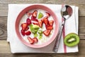 Oatmeal porridge with slices of kiwi, strawberries in pink bowl, spoon, napkin with red stripes on wooden background Top view Flat Royalty Free Stock Photo