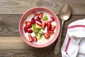 Oatmeal porridge with slices of kiwi, strawberries in pink bowl, spoon, napkin with red stripes on wooden background Top view Flat Royalty Free Stock Photo