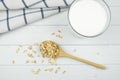 Oatmeal in a wooden spoon, a glass of milk and a tea towel on a light background