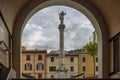 The obelisk of Piazza Mercurio square framed by an arch in the historic center of Massa, Italy