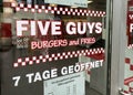 View on restaurant window with lettering of five guys burgers and fries chain with opening hours