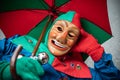 Carnival fool in red-green robe and umbrella rests on the floor