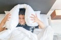 Obese boy lying in bed covering head with pillow because too loud annoying noise. I