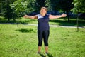 Obese European woman doing morning exercises in nature.