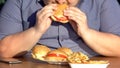 Obese hungry man eating fatty burgers, unhealthy food addiction, overweight
