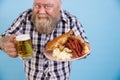 Obese man on blue background, focus on hands with plate of greasy food and beer Royalty Free Stock Photo