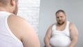 Obese man looking at his mirror reflection, overweight problem and insecurities Royalty Free Stock Photo