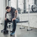 Obese man sitting on bench after exercising with dumbbells at gym Royalty Free Stock Photo