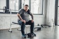 Obese man sitting on bench and Looking At Camera after exercising with dumbbells at gym Royalty Free Stock Photo