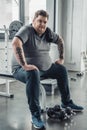 Obese man sitting on bench and Looking At Camera after exercising with dumbbells at gym Royalty Free Stock Photo