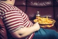 An obese man sitting on the couch eating fast food and drinking sugary drinks bad health habits Generative AI Illustration Royalty Free Stock Photo