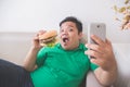 Obese person eating hamburger while using mobile phone Royalty Free Stock Photo