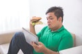 Obese person eating hamburger while using tablet pc Royalty Free Stock Photo