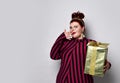 Obese lady in striped dress, crown, earrings. Holding golden gift box tied with ribbon and bow, posing isolated on white