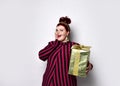 Obese lady in striped dress, crown, earrings. Holding golden gift box tied with ribbon and bow, posing isolated on white