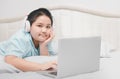 Obese schoolboy lying and wearing headphones to learn online from a laptop