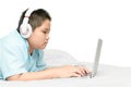 Obese schoolboy lying and wearing headphones to learn online from a laptop on their bed