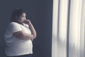 Obese woman looks pensive near the window