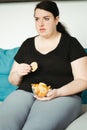 Obese woman sitting on sofa eating unhealthy food Royalty Free Stock Photo