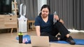 Obese young woman taking a break and drinking water during exercising in living room.