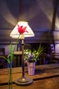 Interior cafe with desk lamp with sconces and red tulip in glass vase and small bouquet of flowers on wooden table Royalty Free Stock Photo