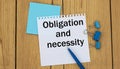 OBLIGATION AND NECESSITY - word written in a notebook on a wooden background with a pen and clamps Royalty Free Stock Photo