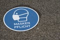 Obligatory mask sign and instruction in German language written on the pavement.