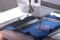 Machine head and embroidery hoop of a modern sewing machine that stitches a magnolia with pink yarn on classic blue boiled wool