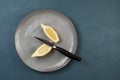 An oblong unusual lemon, cut lengthwise, lies on a gray textured plate. Nearby lies a knife. The trend is eating ugly fruits. Blue