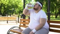 Obsess young man sitting on bench and drinking water after workout outdoors Royalty Free Stock Photo