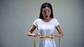 Obsessed woman tightening measuring tape on her waist desire to be slim, bulimia