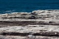 Oceanside rocky cliff top sandstone wave ridges with blue coastal sea in background