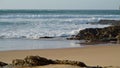 Ocean crashing rocky beach on sunny day. White foamy waves rolling coastline