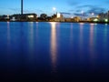 Ocean, night and buildings in port with lights, reflection on calm blue water or holiday location. City at sea in Royalty Free Stock Photo