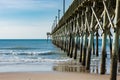 Ocean pier extends out into blue skies and water.