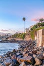 Ocean and rocky shore at the coast with palm trees against blue sky at sunset Royalty Free Stock Photo