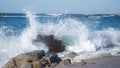 Ocean spray splashing into the air as waves splash over rocks on the beach