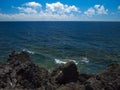 Ocean waves breaking on the rocky coast of hardened lava with caverns and cavities. Deep blue sky with white clouds on the horizon Royalty Free Stock Photo