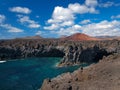 Ocean waves breaking on the rocky coast of hardened lava with caverns and cavities. Deep blue sky with white clouds and mountains Royalty Free Stock Photo