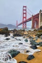 Ocean waves crashing on sandy beach by Golden Gate Bridge on foggy morning