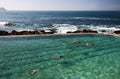 Idyllic and amazing seaside swimming pool, swimmers, landscape of jagged shoreline with rocks, white rushing crashing sea waves Royalty Free Stock Photo