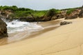 Clean beach sand with ocean waves plashing the shore rocks