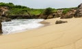 Clean beach sand with ocean waves plashing the shore rocks